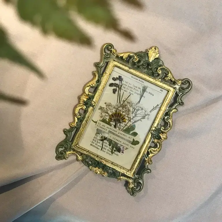 Rechteckiger grün-goldener Barockrahmen mit einer alten Gedicht-Buchseite, verziert mit getrockneten Blüten und Zitaten von Lineativ Studio.