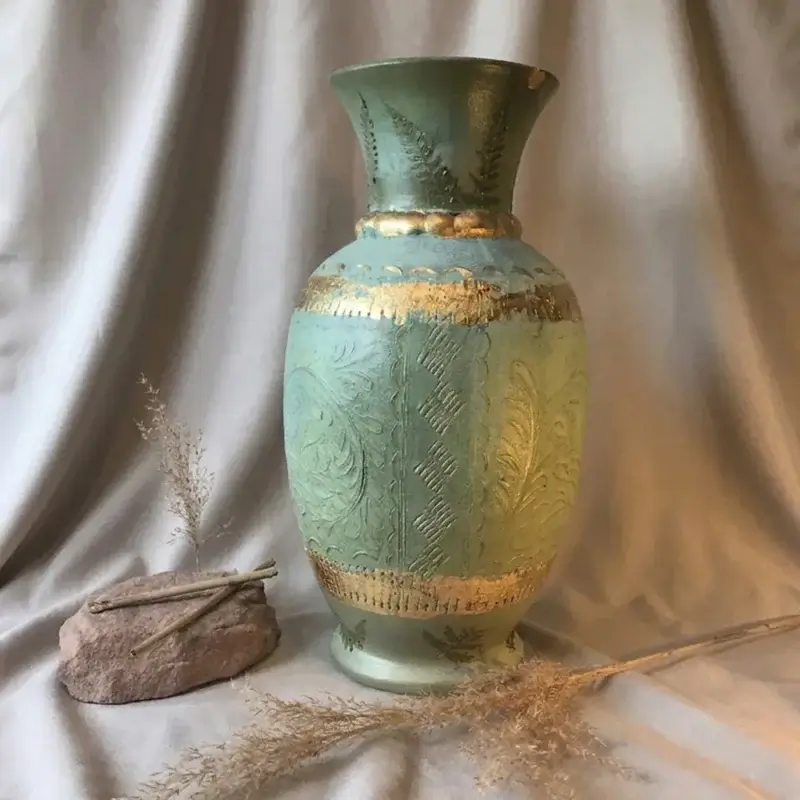 Salbeigrüne Keramikvase im Wabi-Sabi-Stil mit unvollkommener Oberflächentextur, goldenen Akzenten und Farn-Prägungen vor Falten werfendem Leinenstoff.