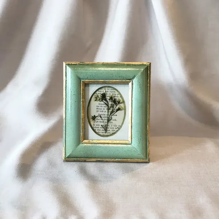 Botanische Naturstudie mit getrockneten Blüten auf einer historischen Buchseite in einem mintgrünen Vintage-Bilderrahmen mit Goldrand von Lineativ Studio.