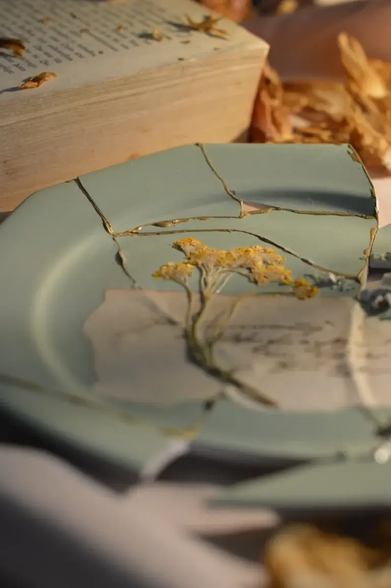 Kintsugi Teller in Salbeigrün mit goldenen Bruchnähten, getrockneter Schafgarbe und alter Buchseite, Lineativ Studio
