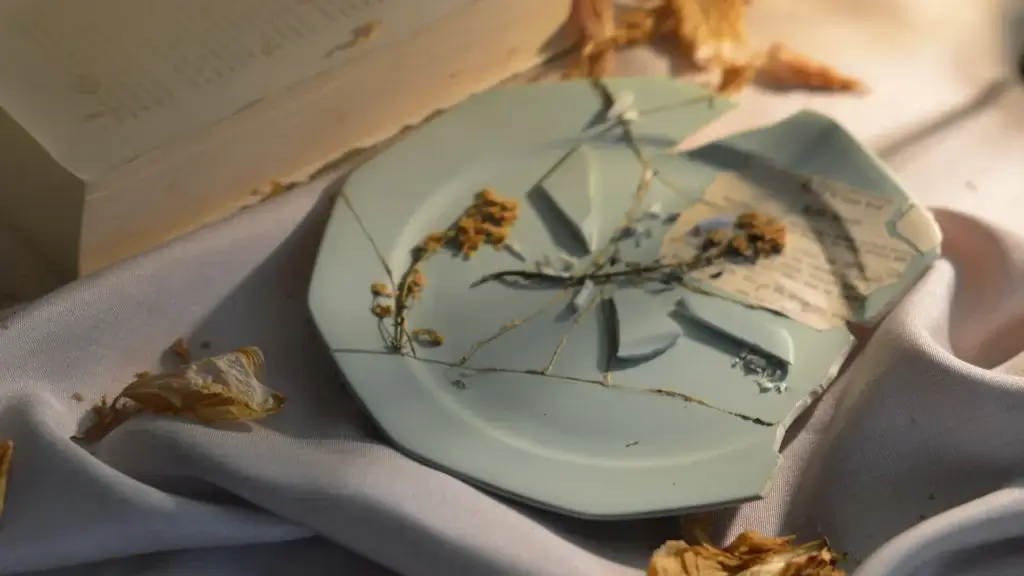 Zerbrochener mintgrüner Keramikteller im Wabi-Sabi-Stil mit getrockneten Blumen und Buchseite auf Stoff vom Lineativ Studio.