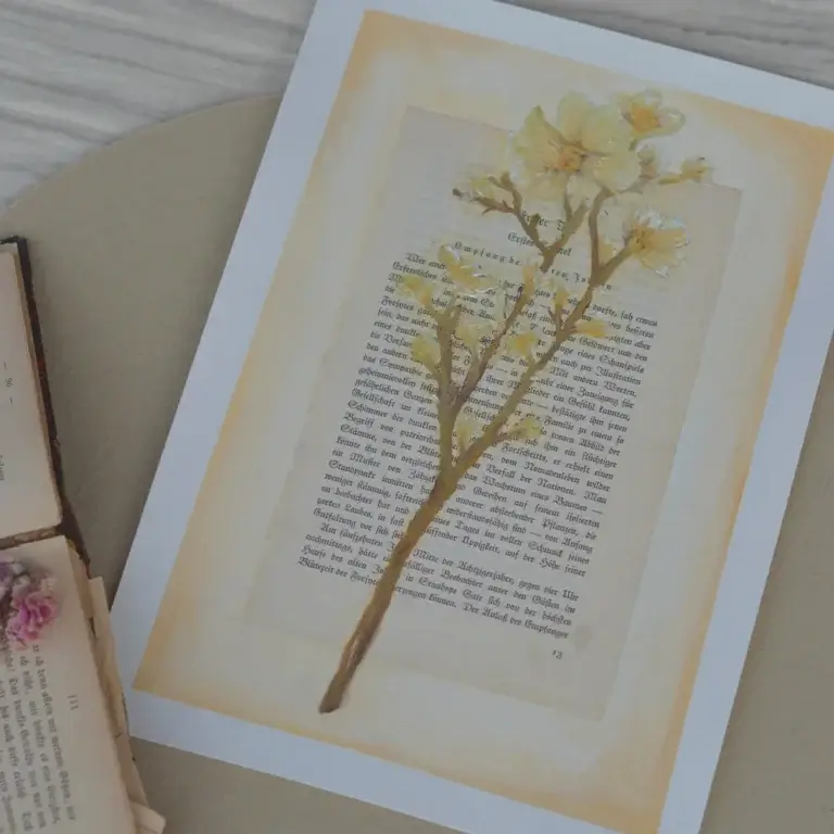 Ein originales Ölgemälde mit leuchtend gelben Blüten und grünen Blättern, fein aufgemalt auf eine historische Buchseite mit Frakturtext. Ein kleiner, filigraner Zweig liegt vertikal über der Mitte der Buchseite.