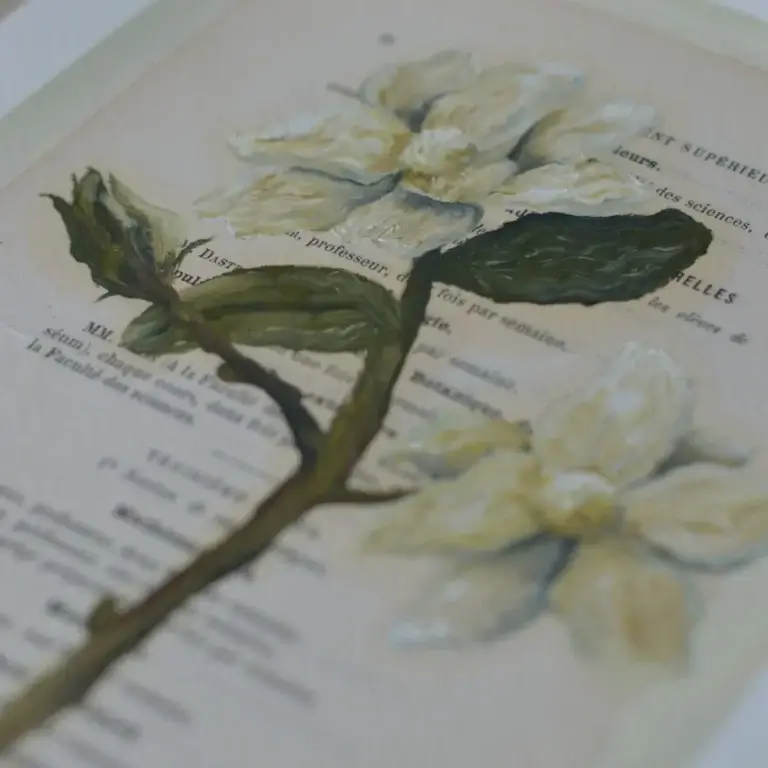 Ein originales Ölgemälde des lineativ studios, das direkt auf eine vergilbte, französische Buchseite gemalt wurde. Das Motiv zeigt detailreiche, cremeweiße Blüten mit realistisch schattierten, grünen Blättern und feinen Stängeln. Der gedruckte französische Text des Buches schimmert an den unbemalten Stellen und durch die transparenten Farbschichten hindurch. Das Bild liegt flach auf einer hellen Oberfläche.