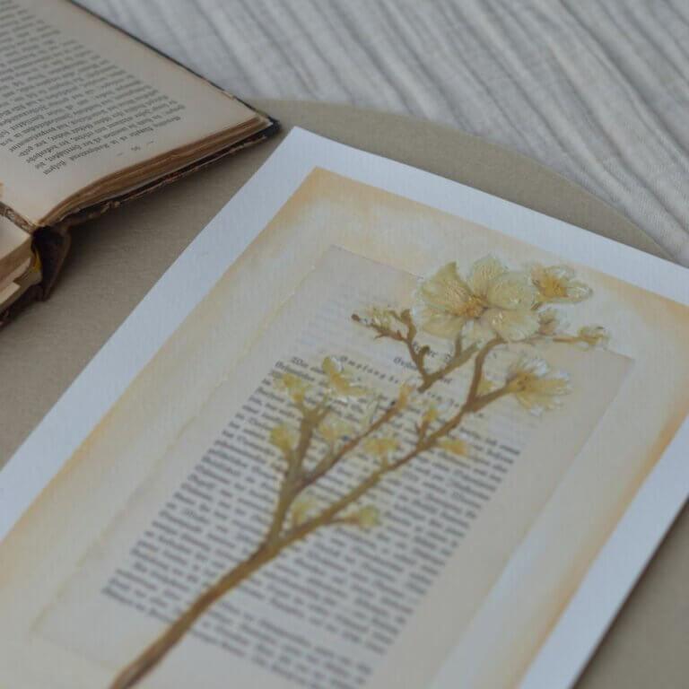 Ein originales Ölgemälde des lineativ studios, das einen filigranen, blattlosen Lebensbaum in Gold- und Ockertönen zeigt. Der Baum ist direkt auf eine vergilbte, antike Buchseite mit gedruckter deutscher Frakturschrift gemalt. Das Kunstwerk liegt flach auf einer hellen Unterlage, während im Hintergrund ein weiteres aufgeschlagenes Buch zu sehen ist