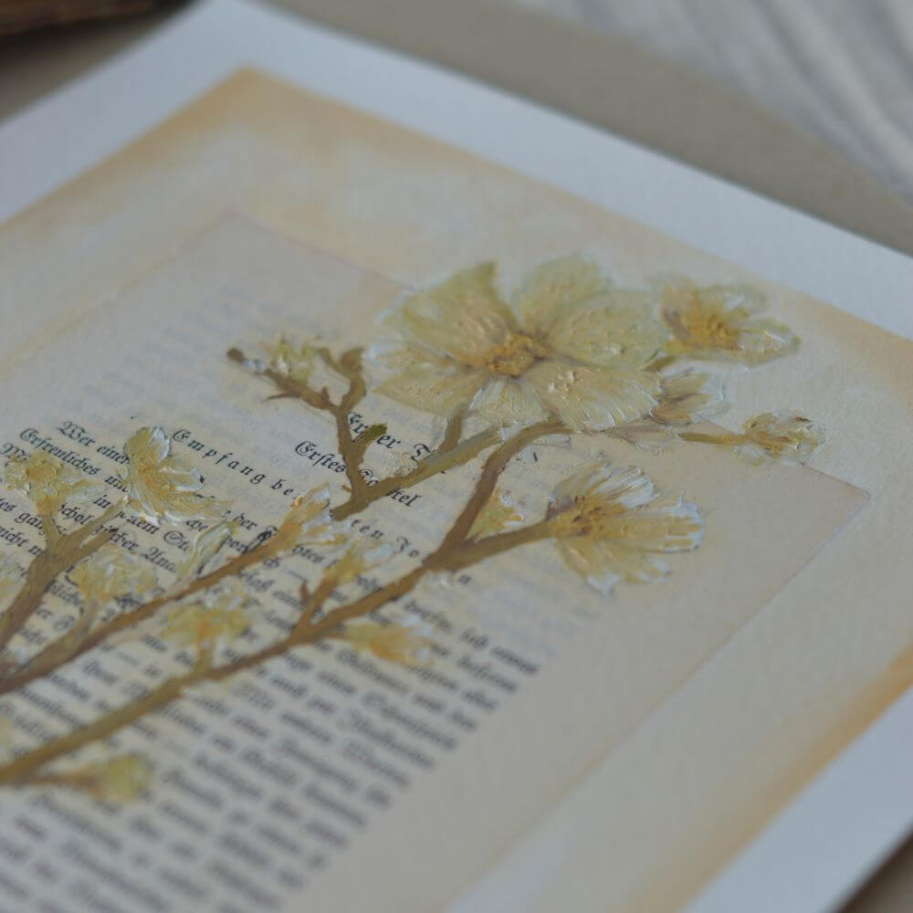 Ein originales Ölgemälde des lineativ studios, das einen filigranen, blattlosen Lebensbaum in Gold- und Ockertönen zeigt. Der Baum ist direkt auf eine vergilbte, antike Buchseite mit gedruckter deutscher Frakturschrift gemalt. Das Kunstwerk liegt flach auf einer hellen Unterlage, während im Hintergrund ein weiteres aufgeschlagenes Buch zu sehen ist