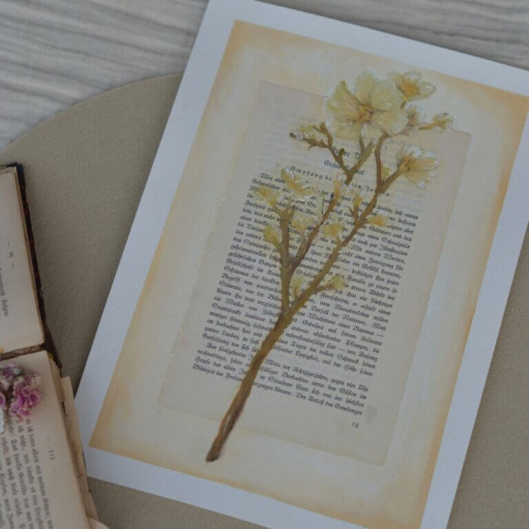 Ein originales Ölgemälde des lineativ studios, das einen filigranen, blattlosen Lebensbaum in Gold- und Ockertönen zeigt. Der Baum ist direkt auf eine vergilbte, antike Buchseite mit gedruckter deutscher Frakturschrift gemalt. Das Kunstwerk liegt flach auf einer hellen Unterlage, während im Hintergrund ein weiteres aufgeschlagenes Buch zu sehen ist