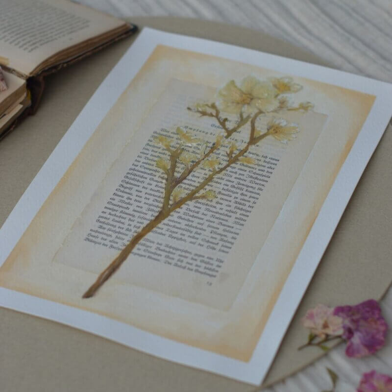 Ein originales Ölgemälde des lineativ studios, das einen filigranen, blattlosen Lebensbaum in Gold- und Ockertönen zeigt. Der Baum ist direkt auf eine vergilbte, antike Buchseite mit gedruckter deutscher Frakturschrift gemalt. Das Kunstwerk liegt flach auf einer hellen Unterlage, während im Hintergrund ein weiteres aufgeschlagenes Buch zu sehen ist